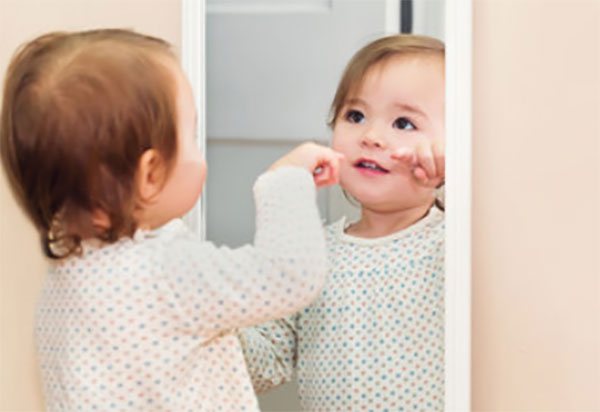 Дівчинка стоїть перед дзеркалом з відкритим ротиком