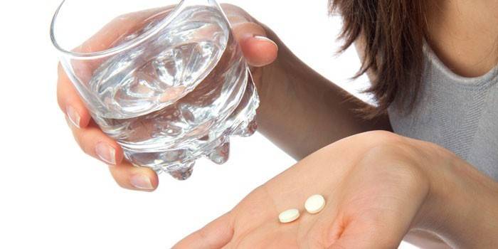 Дівчина тримає таблетки на долоні і стакан води в руці