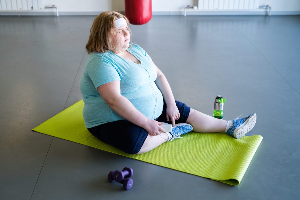Женщина с избыточным весом сидит на коврике для йоги и отдыхает после фитнес-тренировки