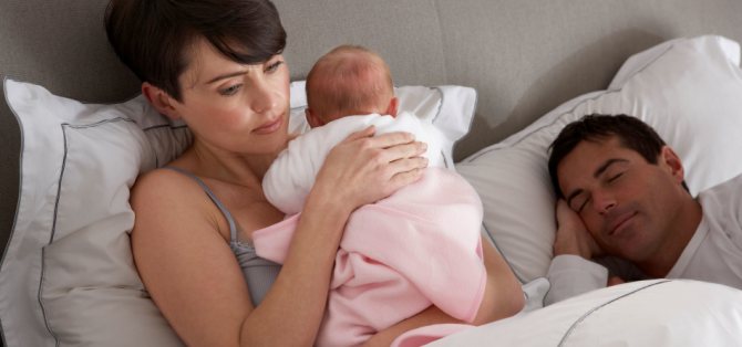 Втомлена молода мама тримає малюка на руках